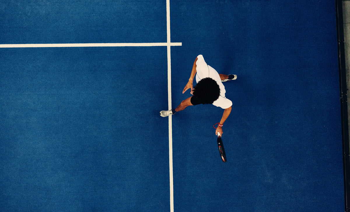 Overhead view of a padel player alone on a blue court, the service lines crossing beside them