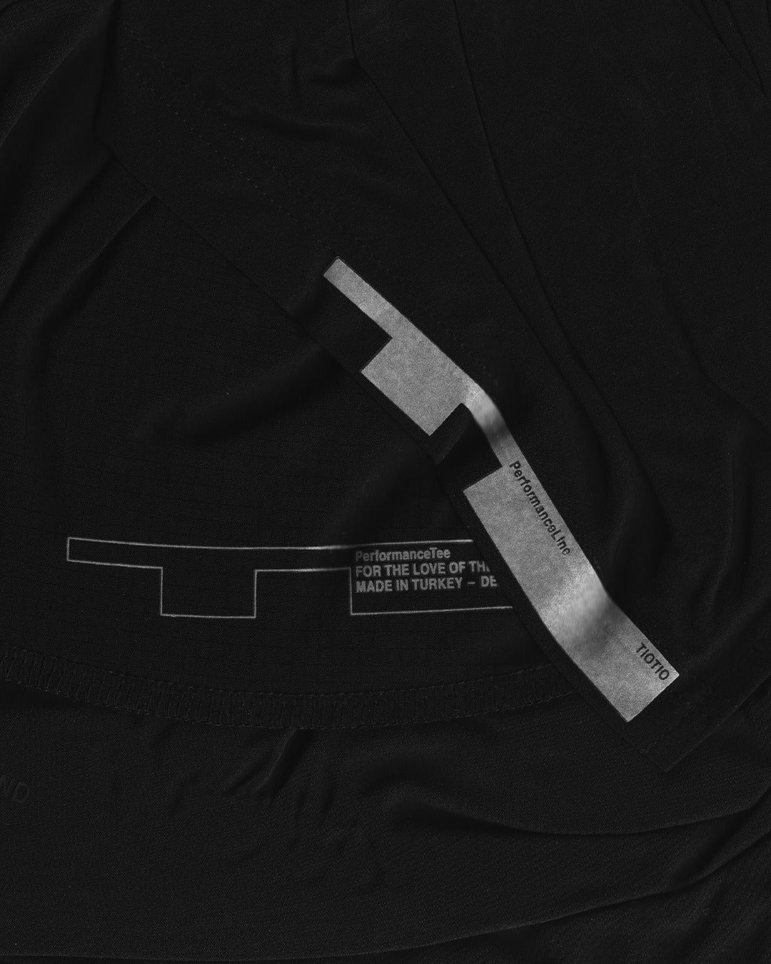 Printed care label and woven TIOTIO tab on the inside of the black Performance Tee