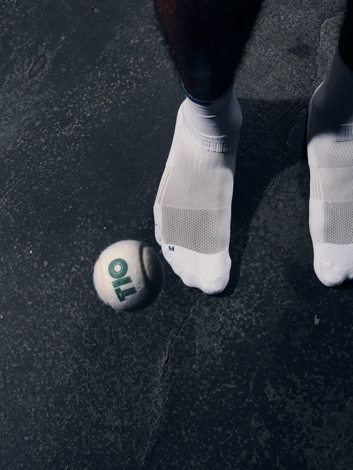 White TIOTIO Performance Socks on a wet court surface next to a TIO ball, seen from above